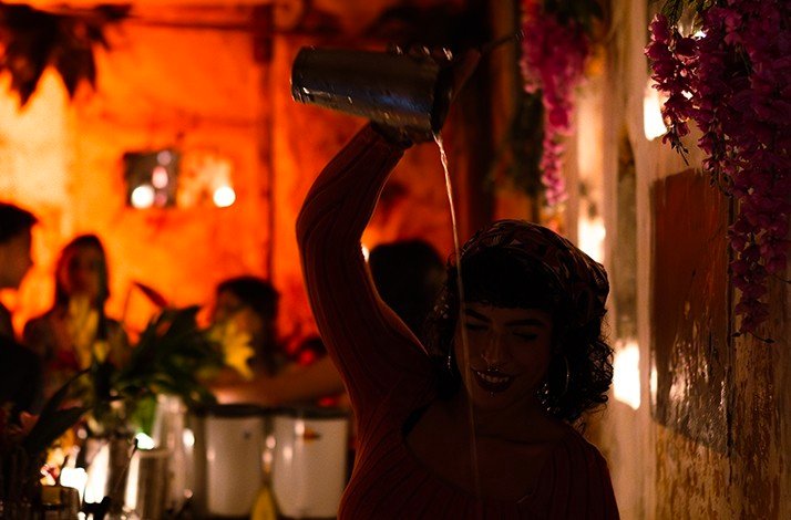 A girl in red light pours a cocktail from a shaker at La Factoria.
