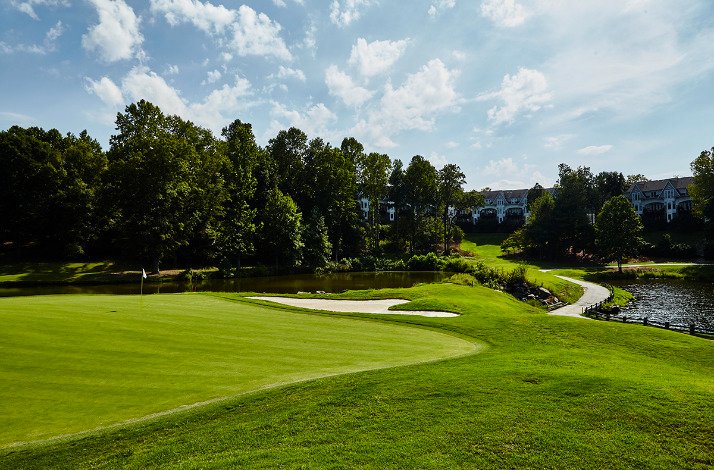 A golf course at TPC surrounded by trees under a clear blue sky.
