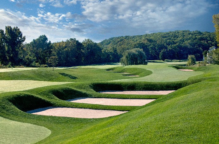 A golf course at TPC surrounded by trees under a clear blue sky.