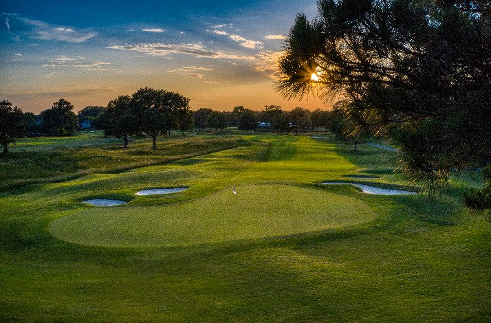 A golf course at TPC surrounded by trees under a clear blue sky.