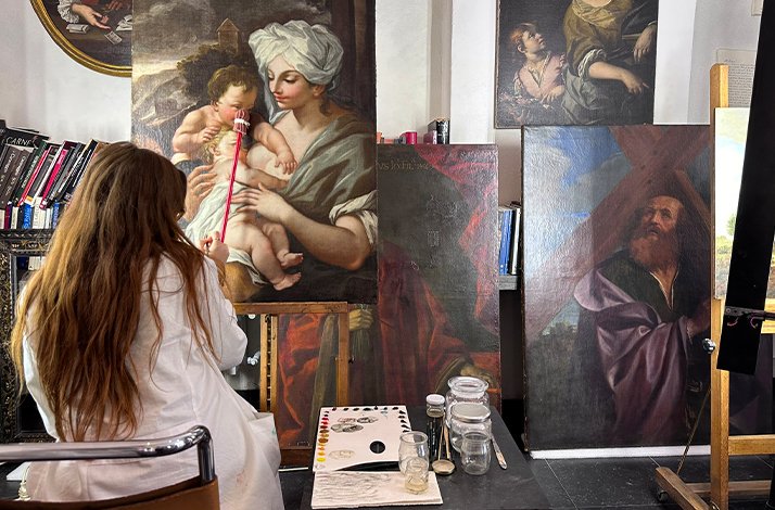 Restorer at work photographed from the back. The worker is surrounded by paintings