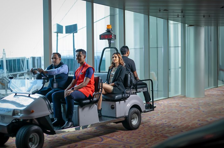 A woman along with Pranaam Meet & Greet services staff rides a Dedicated Branded Buggy.