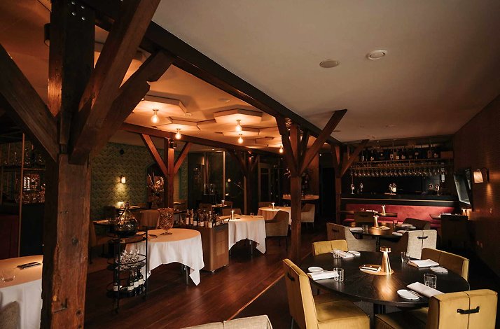 Elegant restaurant interior at Hotel & Spa Savarin, featuring warm lighting, wooden beams, and tables set for a luxurious dining experience.
