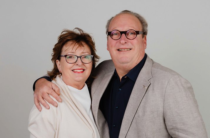 Millie Patrick Savarin in formal attire, standing together with an arm around each other, against a plain light background.