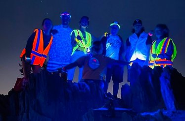 Group of people with glowing accessories and UV flashlights discovering the Arizona desert on a unique after-dark expedition.