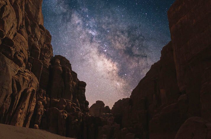  The Milky Way stretches across the night sky above a vast canyon, illuminated by countless stars.