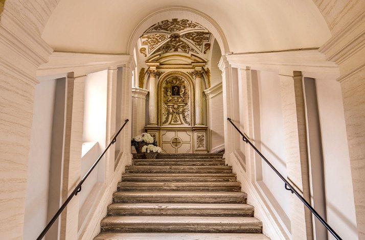 A staircase with a wooden railing, featuring a round clock mounted on the wall beside it.