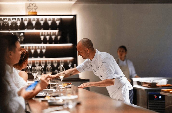 The chef of restaurant PRU serving the guests sitting in front of cooking area