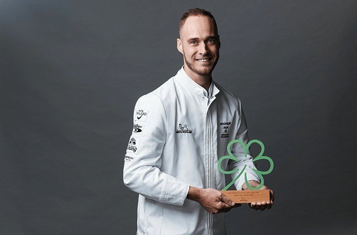 Chef with an award in form of a green 5 leaves flower.