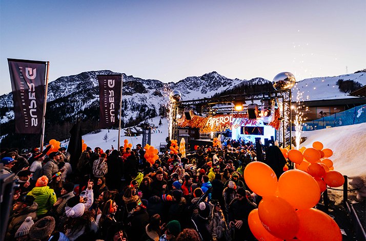 A lively Super G outdoor party in Courmayeur, shows a large crowd enjoying music.