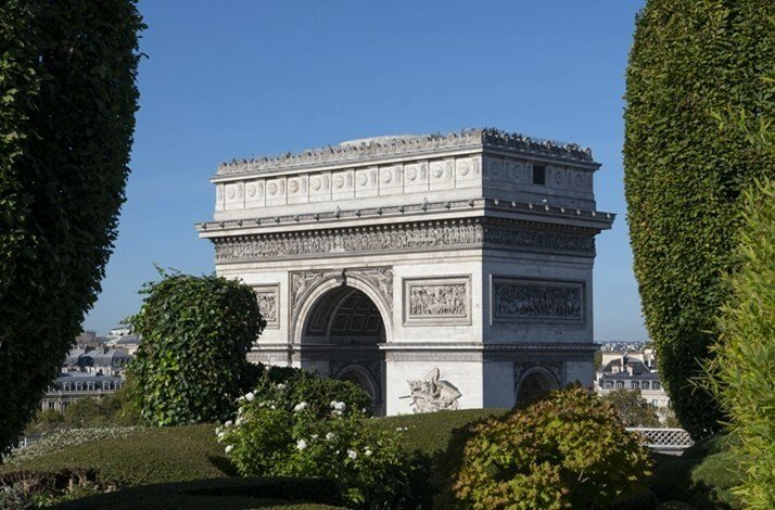 A green garden on a sunny day. The Arc de Triomphe is in the background.