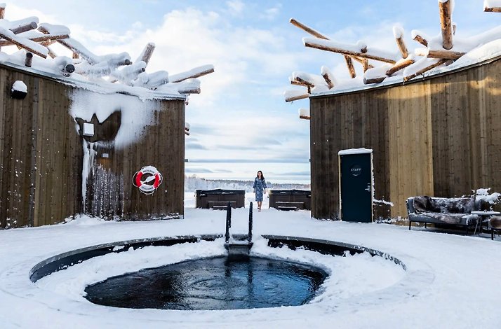 A person stands before a hot tub surrounded by snow at Ecolyx Arctic Bath winter spa