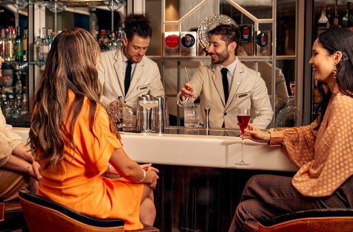 A group of bartenders preparing a cocktail for a group of womans