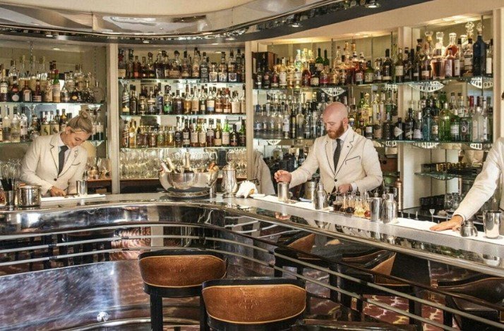 Three bartenders in white suits working on the bar of The Savo