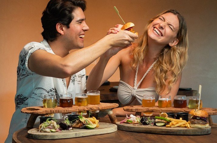 A couple enjoying a small menu at Cervecería Tulum Brewery Restaurant with different Pints, the girl is laughing