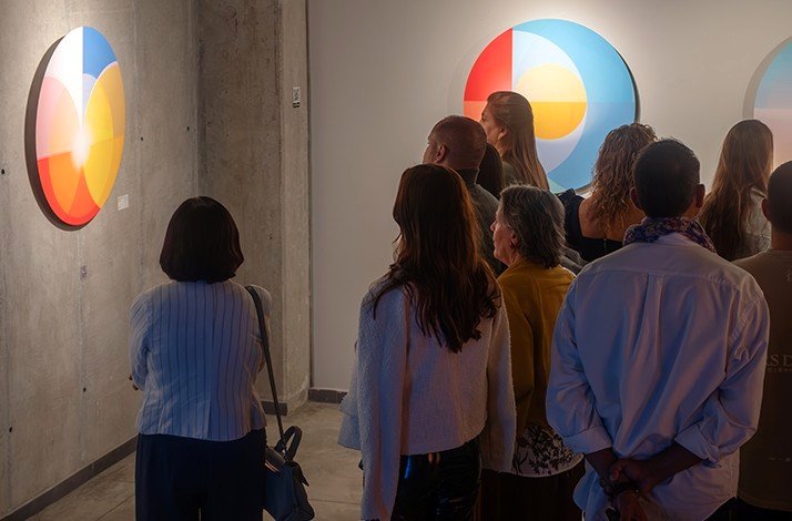 A group of people look at geometric paintings in bright colours at Zehn Living.