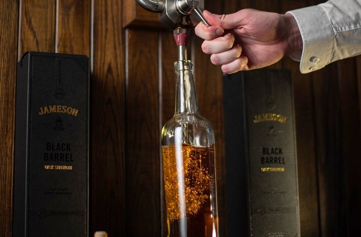 A man pours whiskey from a bottle into a glass, showcasing a moment of preparation for a drink at the Midleton Distillery.