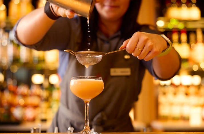 A woman filtering a cocktail through a fine strainer