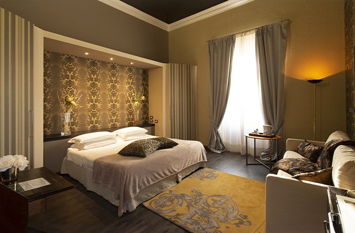 A luxurious hotel room with a large bed, couch and natural lighting