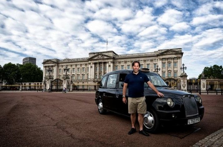 A tourist posing for the phono near the Buckingham palace standing by the black cab