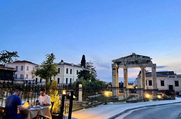 Two people dining at a terrace overlooking Ancient Roman columns in Plaka, Athens.