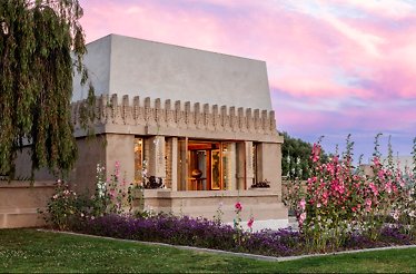 Outdoor exterior of Frank Lloyd Wright's Hollyhock House, surrounded with greenery and flowers.