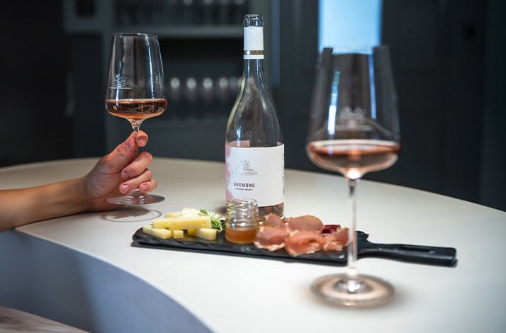 Hand holding glass at table with rose wine and snacks at Sella & Mosca winery.