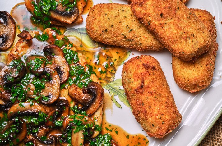 A plate featuring sautéed mushrooms alongside a piece of breaded meat, garnished with herbs.