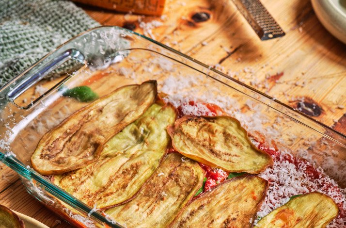 A glass dish filled with neatly arranged slices of eggplant, showcasing its rich purple color and smooth texture.