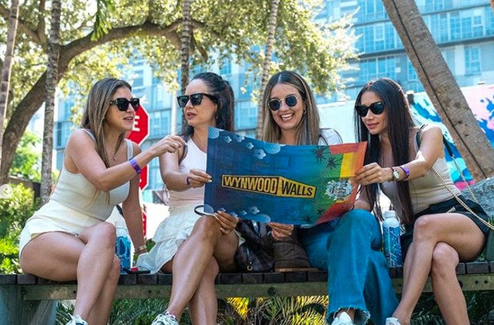 Four girls sitting on the bench and looking at Wynwood Walls poster.