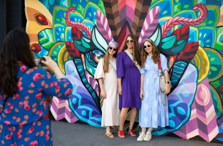 Three women taking pictures in front of a creative wall