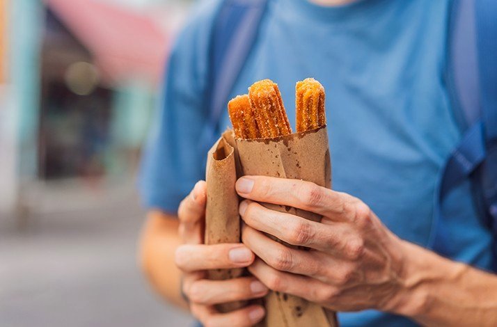 A person holding sweet street food wrapped in paper bag.
