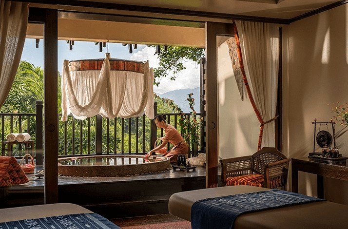 A woman relaxes in a spa room, enjoying a serene view through large windows.