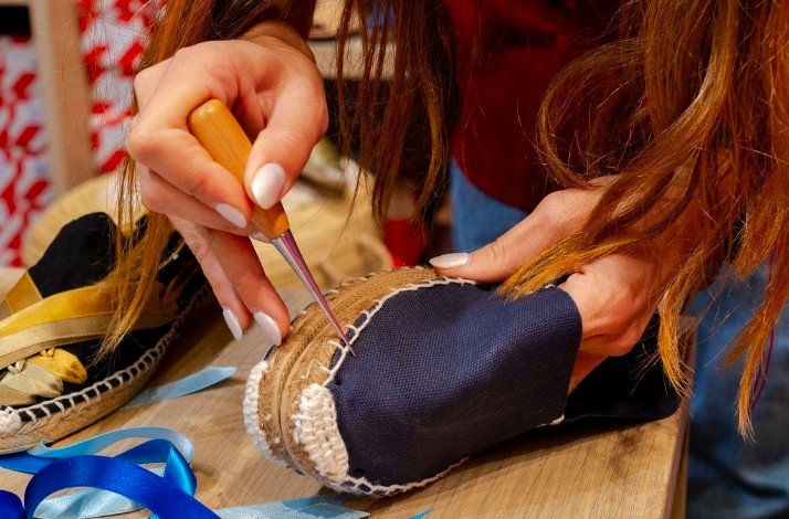 A woman is using scissors to cut a pair of shoes on a table.