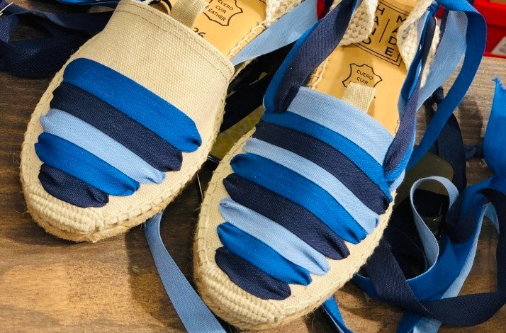 A pair of blue and white striped espadrilles displayed side by side on a neutral background.