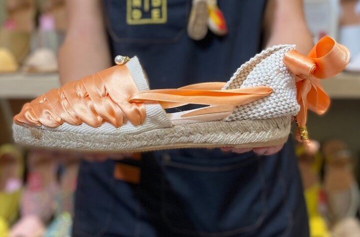 A person showing her handmade summer shoes in white with orange ribbon.
