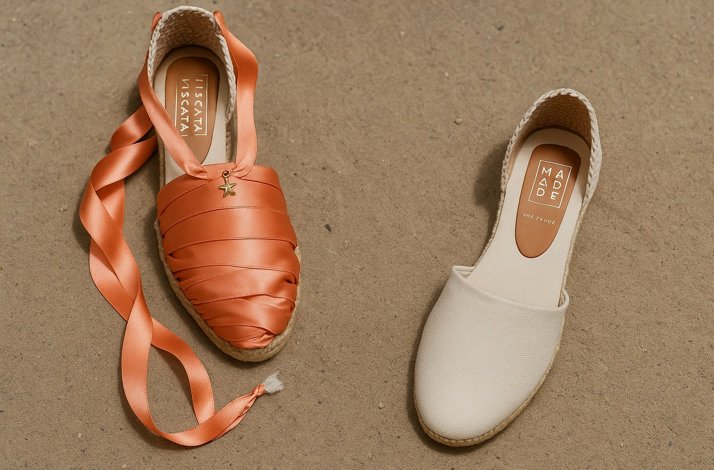Two pairs of summer shoes on sand - one decorated with orange ribbon, one with no ribbons..