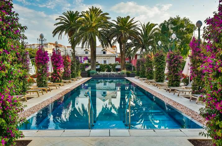 A serene pool encircled by vibrant green plants and tall palm trees, creating a tropical oasis atmosphere.