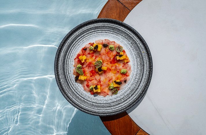 A plate of food on a table beside a pool at YONA Beach Club