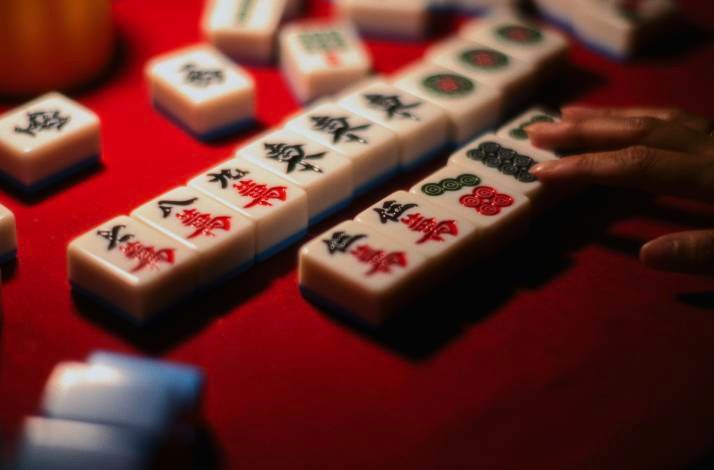 A close-up of a player arranging Mahjong tiles during a game on a red table.