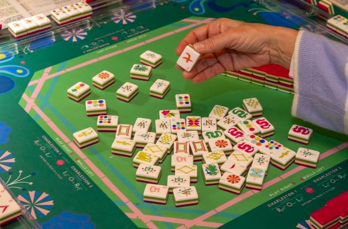 A player picking a Mahjong tile from a vibrant game board setup.