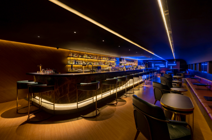 Interior of a sleek, modern bar with warm lighting and a long illuminated counter.