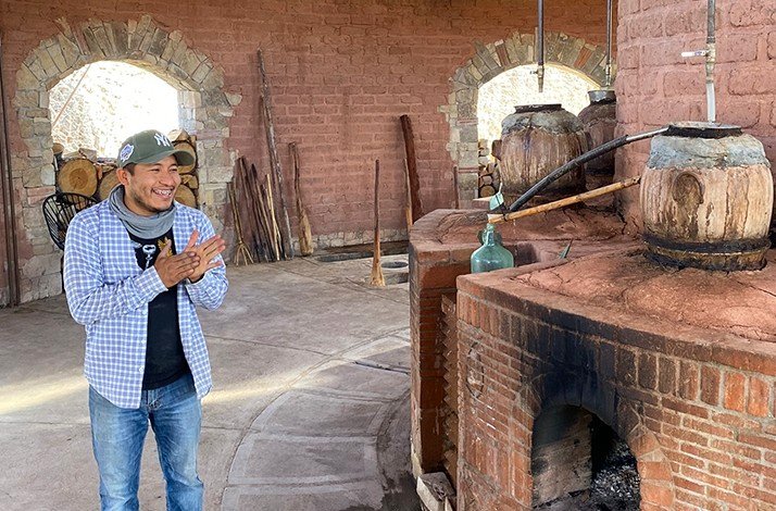A man stands next to a rustic brick oven used for distillation.