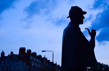A silhouette of a man, likely a statue of Sherlock Holmes, is depicted against a twilight sky, with buildings in the foreground.