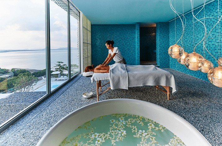 A person receiving a massage in a serene room with a panoramic view of the ocean.