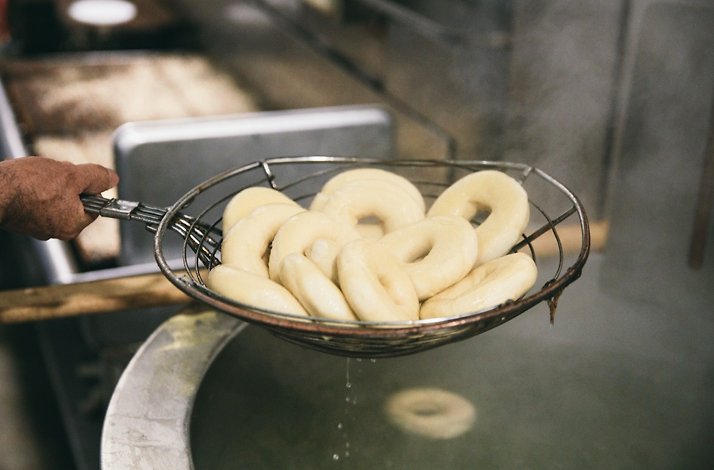 Baker's hand lifting freshly boiled bagels from a water bath using a wire skimmer at Russ & Daughters kitchen.
