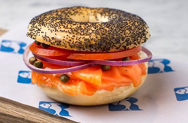 Poppy seed bagel layered with smoked salmon, cream cheese, tomato, red onion, and capers on Russ & Daughters paper.