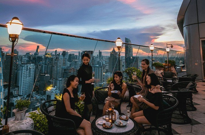 A group of girls chat on the terrace of Park Hyatt Bangkok's plush Penthouse Bar + Grill.