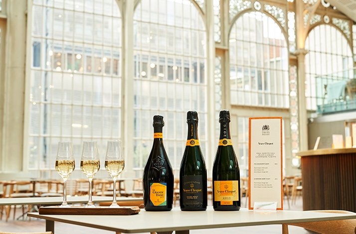 Table with Veuve Clicquot champagne bottles and glasses in a bright, airy lounge.