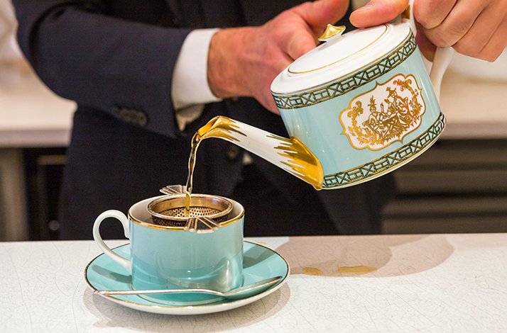 A person pouring tea in an elegant turquoise tea cup at the Fortnum & Mason department store.